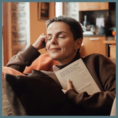Mujer relajada en un sofá, sosteniendo un libro, con expresión serena.
